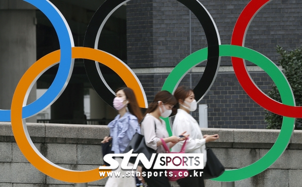 8일 일본 도쿄에서 코로나19 확산 방지를 위해 마스크를 쓴 사람들이 도쿄 올림픽 오륜 조형물 앞을 지나가고 있다. 사진｜뉴시스/AP